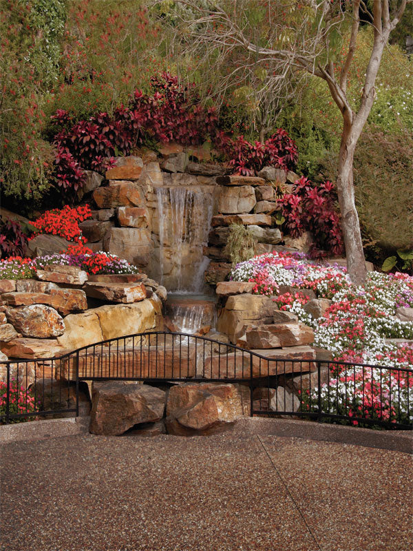 Vivid floral garden backdrop with cascading stone waterfall and scenic bridge.