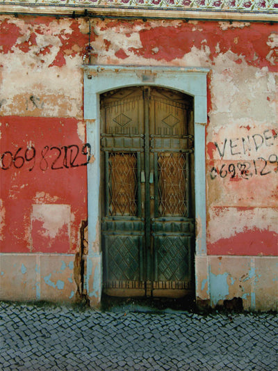A rustic photography backdrop with a worn wooden door and distressed stucco wall.
