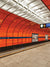 Orange Wall Metro Station Photography Backdrop - Vibrant orange walls and sleek design of a Munich metro station with blue stripe, black lines, and bright fluorescent lighting.