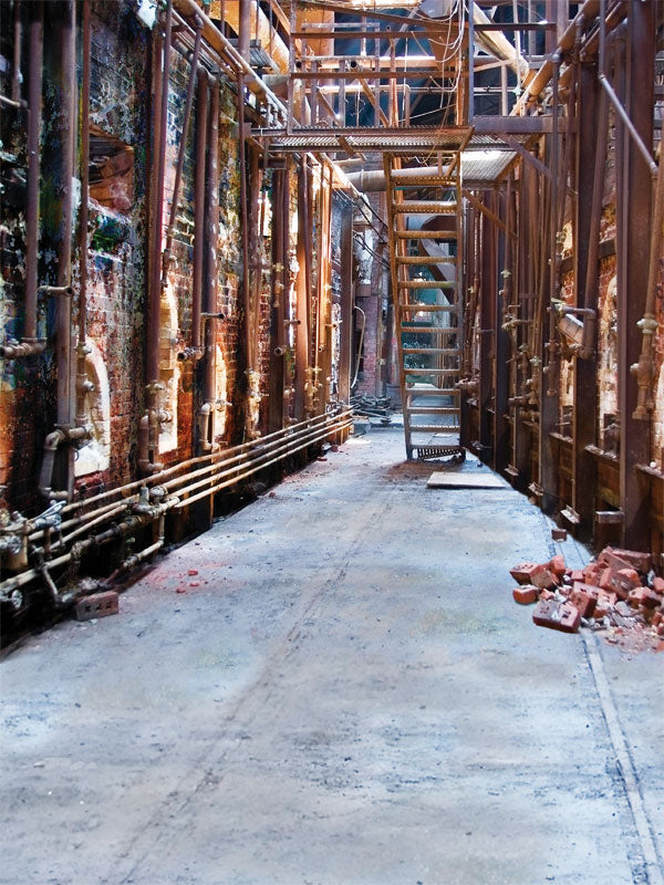 Creepy abandoned warehouse with pipes, debris, and metal stairwell for horror portraits.
