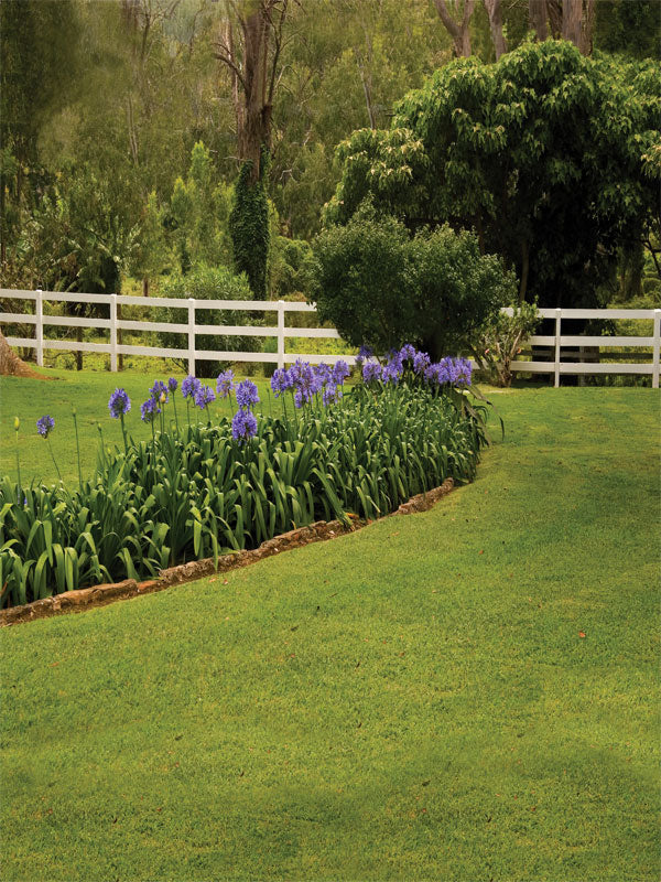 Vivid green grass with white fence and floral edge in a ranch setting.