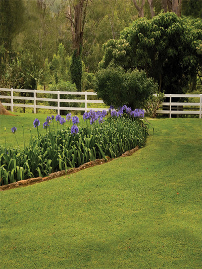 Vivid green grass with white fence and floral edge in a ranch setting.