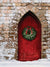 Red Rustic Christmas Door Photography Backdrop - Red rustic door adorned with a Christmas wreath, set in a stone archway with a snow-covered ground, ideal for holiday photoshoots.