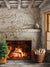 Rustic Fireplace Photography Backdrop - A cozy stone fireplace with a roaring fire, decorated with a small evergreen tree and a basket of logs, perfect for holiday or winter photography.