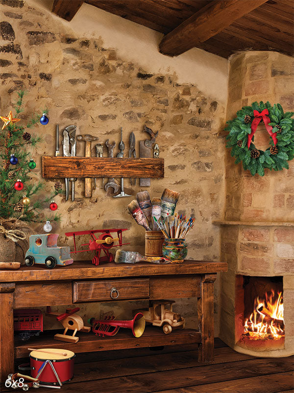 Santa's Workshop Toy-Making Corner Photography Backdrop - A cozy Santa's workshop photography backdrop featuring a rustic workbench with wooden toys, a small Christmas tree, and a warm fireplace.
