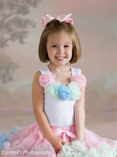 Smiling young girl in pastel ruffle dress poses in front of a light floral Sheffield photography backdrop, perfect for whimsical children's portrait sessions.