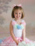 Smiling young girl in pastel ruffle dress poses in front of a light floral Sheffield photography backdrop, perfect for whimsical children's portrait sessions.