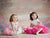 Two young girls in pastel tutus sit cheerfully in front of a soft pastel garden backdrop—perfect for whimsical children’s portraits and springtime photography.
