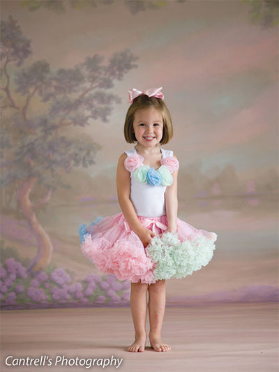 Close-up of smiling girl in pastel outfit with pink bow against soft floral garden background—ideal for charming child portraiture.