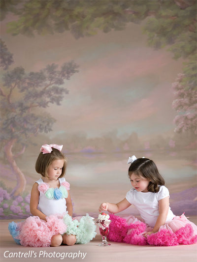 Two girls in pastel tutus share a sweet moment with a sundae, seated in front of a dreamy spring garden backdrop—great for styled children’s portraits.