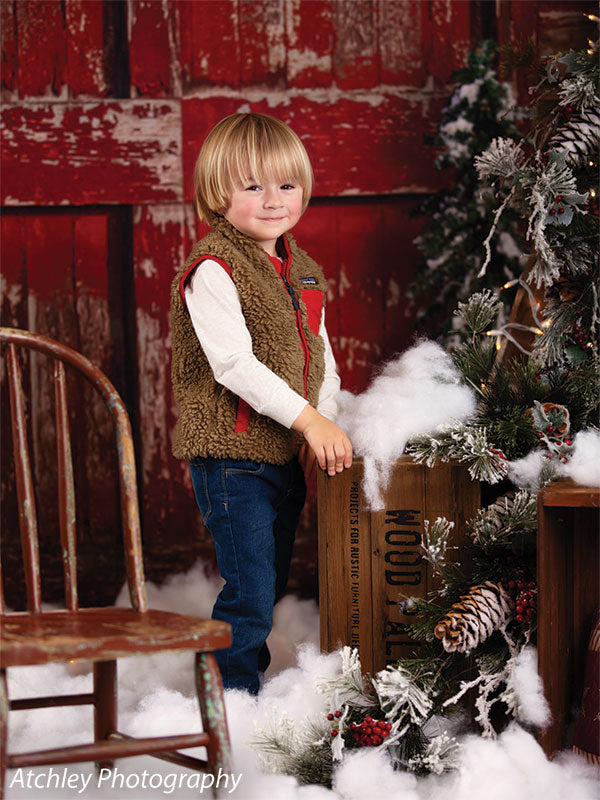 Festive photography backdrop with a snow-covered red barn door, pine trees, and classic holiday decor.