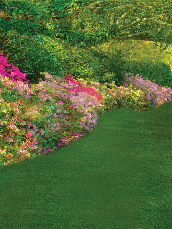 Vibrant pink and purple flowers line a garden path under a sunlit canopy of trees.