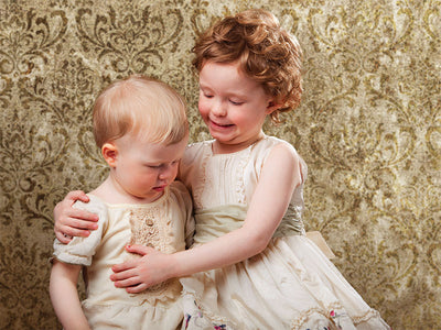 Two young children in heirloom-style outfits pose in front of a richly patterned gold damask backdrop—perfect for family portraits, traditional children's photography, and vintage studio sessions.