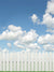 Sunny Skies with White Picket Fence Photography Backdrop - Photography backdrop featuring a white picket fence against a bright blue sky with white clouds, ideal for children's and family photoshoots.