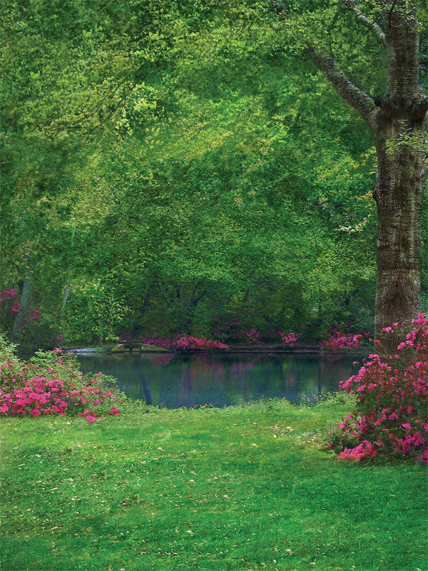 A peaceful lakeside photography backdrop with lush green trees, soft pink flowers, and a reflective water surface.