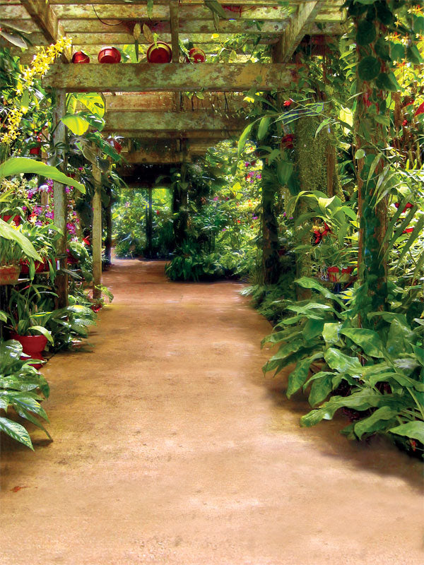 A lush tropical garden photography backdrop featuring a shaded pergola walkway surrounded by vibrant green plants and hanging florals.