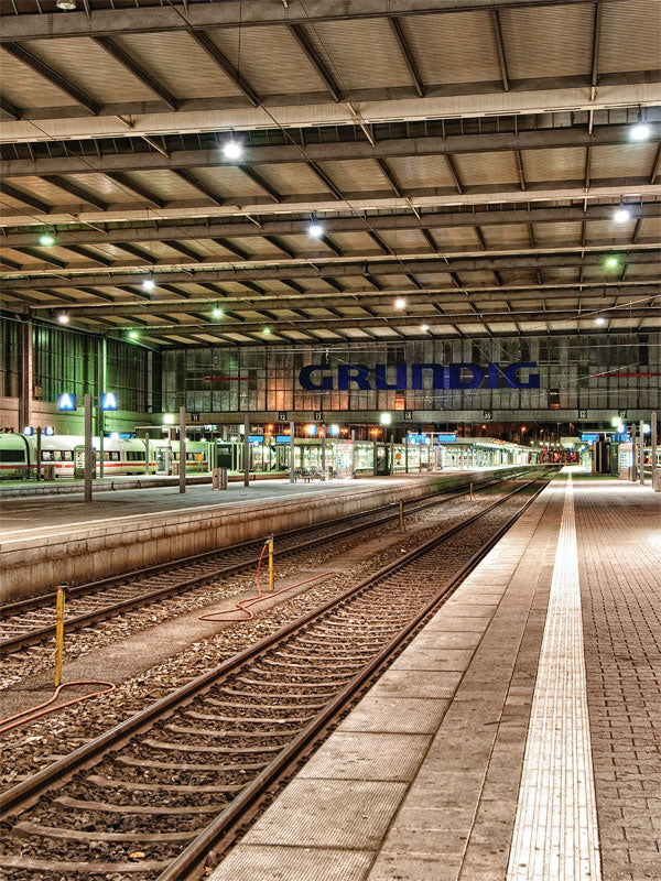 Urban Train Station Photography Backdrop - Expansive train station with multiple tracks under a high industrial ceiling, illuminated by bright overhead lights and the GRUNDIG sign.