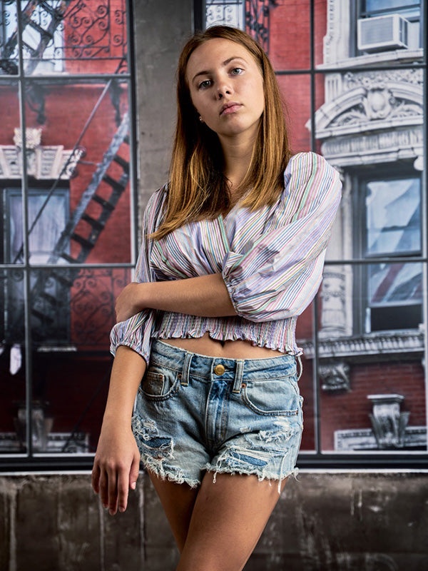 Teen model posing in front of industrial-style red brick loft windows—perfect for senior and editorial photographers.
