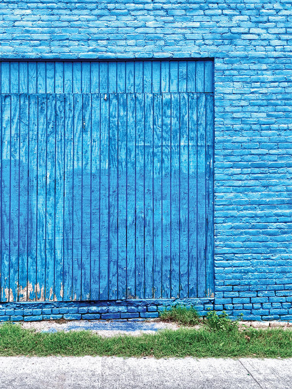 Vibrant Blue Brick and Wood Wall Backdrop - Vibrant blue brick wall with a weathered blue wooden sliding door, and a strip of green grass in front.