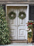 Vintage Christmas Door Photography Backdrop - A vintage Christmas door photography backdrop featuring white double doors with green wreaths, a snow-covered tree, and holiday props like a sled and ice skates.