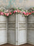 Vintage Floral Panel Photography Backdrop - Vintage paneled screen with intricate carvings, topped with a lush garland of pink and peach roses, set against a textured wall for photography backdrop.