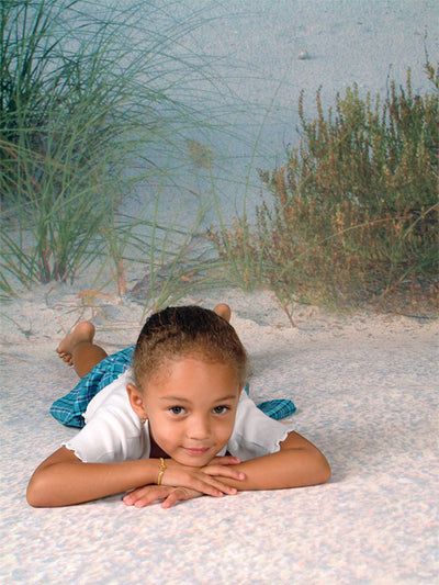 A professional studio backdrop depicting a serene beach with white sand, deep blue ocean waters, and a cloud-speckled sky.
