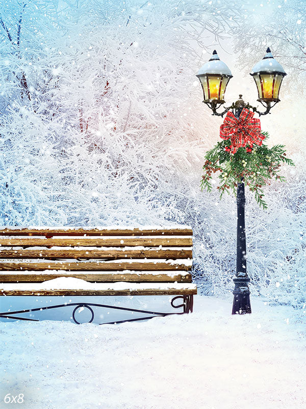 Winter Park Bench and Lantern Photography Backdrop - Photography backdrop featuring a serene winter park scene with a rustic bench and a vintage lantern adorned with a festive wreath amidst snow-covered trees.