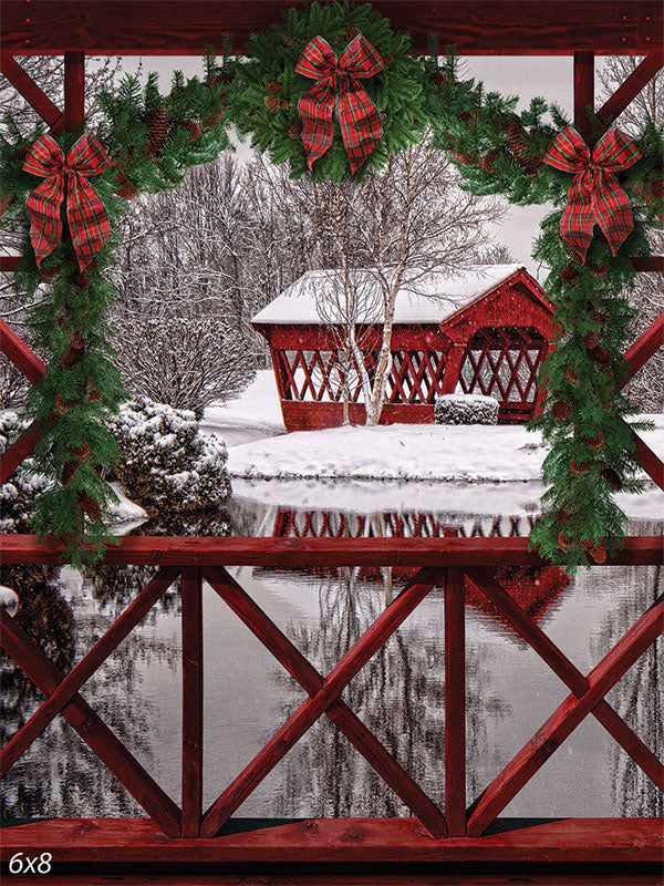 Winter Wonderland Bridge Photography Backdrop - Photography backdrop depicting a winter scene with a red covered bridge, snow-covered landscape, and festive garlands and bows.