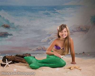 Child in mermaid costume posed in front of an ocean backdrop with beach props, ideal for creative dance or themed portrait sessions.