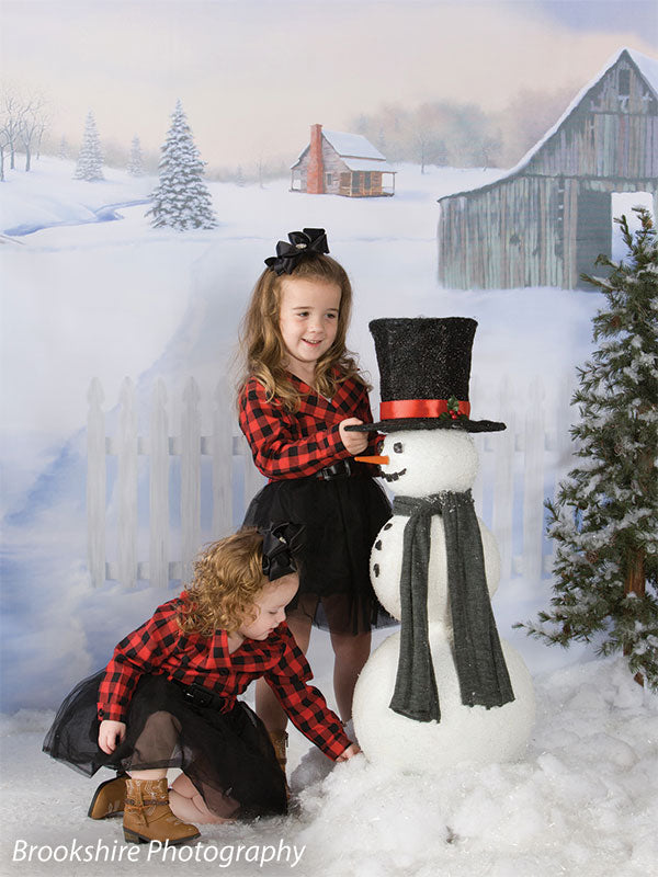 Two young girls play with a snowman in front of the Country Holiday backdrop, evoking a charming winter farm scene.