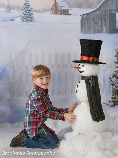A young boy smiles beside a snowman in front of the printed snowy Country Holiday backdrop, perfect for seasonal studio photos.