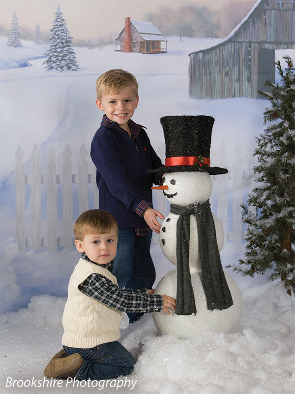 Two brothers pose with a snowman in front of a rustic farm winter backdrop, ideal for Christmas card photography.