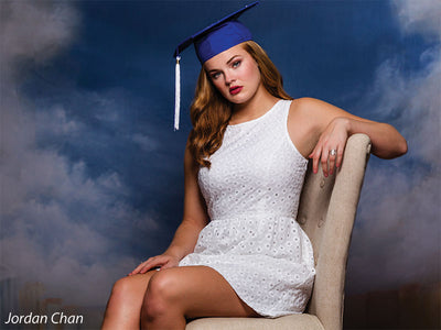 Young woman in cap and gown posed against a Venice-inspired backdrop with painterly sky, perfect for school and editorial portraits.