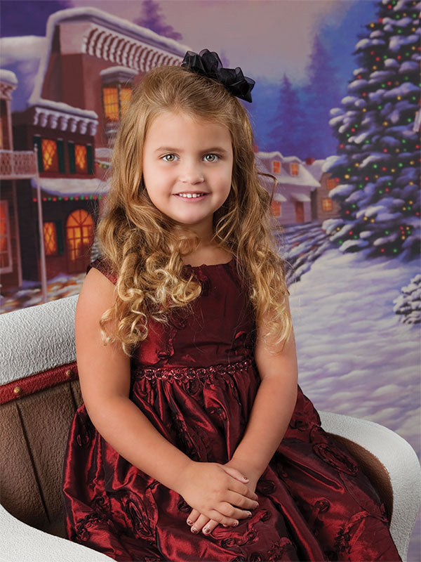 Holiday Shops printed backdrop creates a cheerful seasonal scene behind a smiling young girl in a holiday dress.