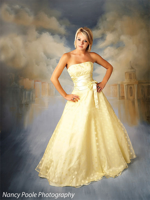 Young woman in elegant yellow dress against a classic European cityscape backdrop, perfect for prom, senior, or fashion portraits.