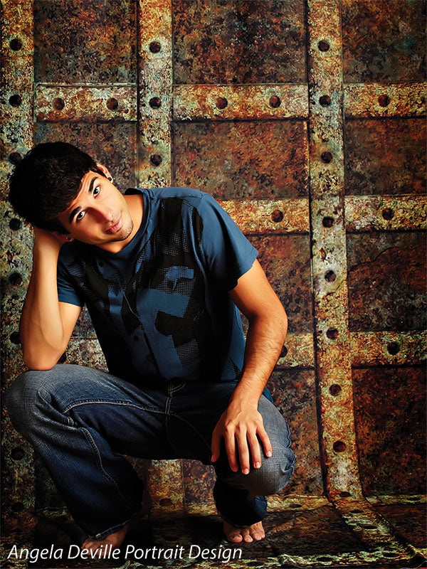 Teen male in relaxed pose in front of a distressed riveted steel backdrop, perfect for moody senior photography.