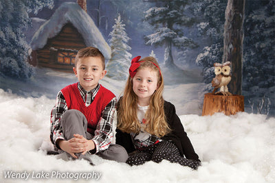 Two children pose in front of the Holiday Cottage backdrop, surrounded by snowy textures and a glowing winter forest scene.