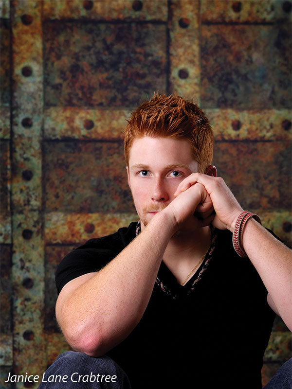 Male senior portrait posed against a rusty rivets backdrop, delivering strong industrial texture and urban mood.