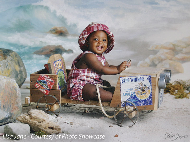 Smiling infant in playful seaside setup with waves and rustic beach props, ideal for newborn and toddler portrait sessions.