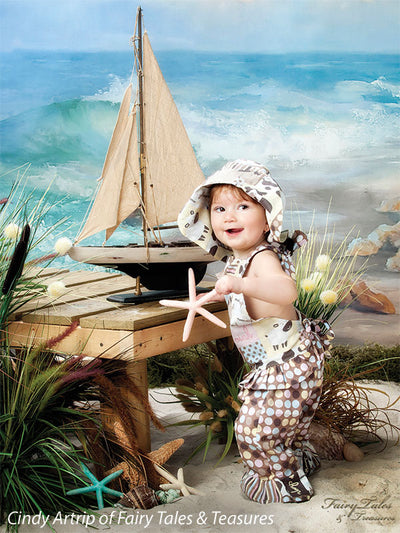 Toddler portrait with sailboat and seagrass against a painted ocean scene, perfect for newborn and family beach-themed setups.