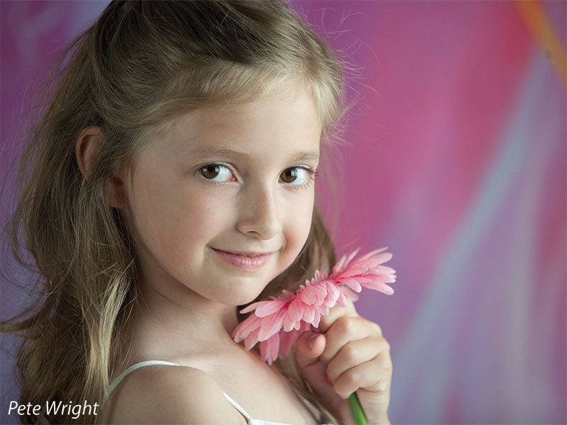 Close-up of young girl with daisy against a swirling pink and lavender backdrop, ideal for delicate children's photography.