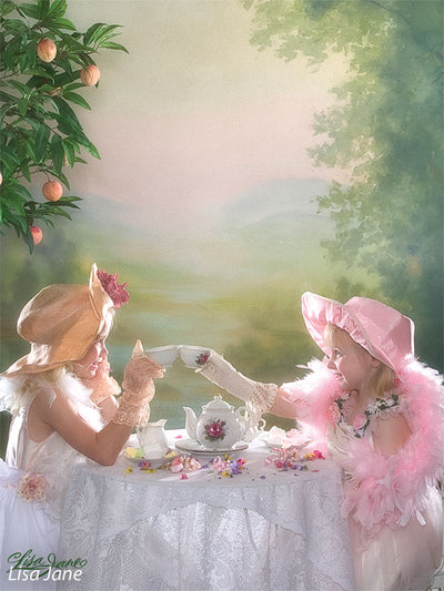 Printed backdrop with soft valley view and gentle trees, used in a stylized tea party scene with two young girl models in vintage dresses.