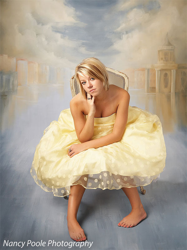 Studio image of a young woman in formal gown seated before a painterly Venice skyline, ideal for glamour or graduation sessions.