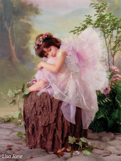 Printed photography backdrop with natural woodland hues and dreamy valley view, styled with a child model in fairy wings sitting on a tree stump.