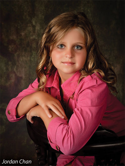 Young model in pink shirt poses in front of the Scrolled Backdrop, emphasizing its subtle scroll accents and rich vintage tones for classic children’s portraits.