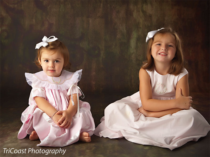 Two children posed in front of the Scrolled Backdrop, illustrating its warm, vintage color palette and subtle scroll design for sibling and family sessions.