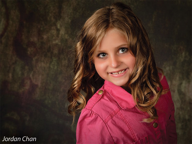 Young model smiling in front of the Scrolled Backdrop, showing how its vintage swirl accents add texture to children’s portrait photography.