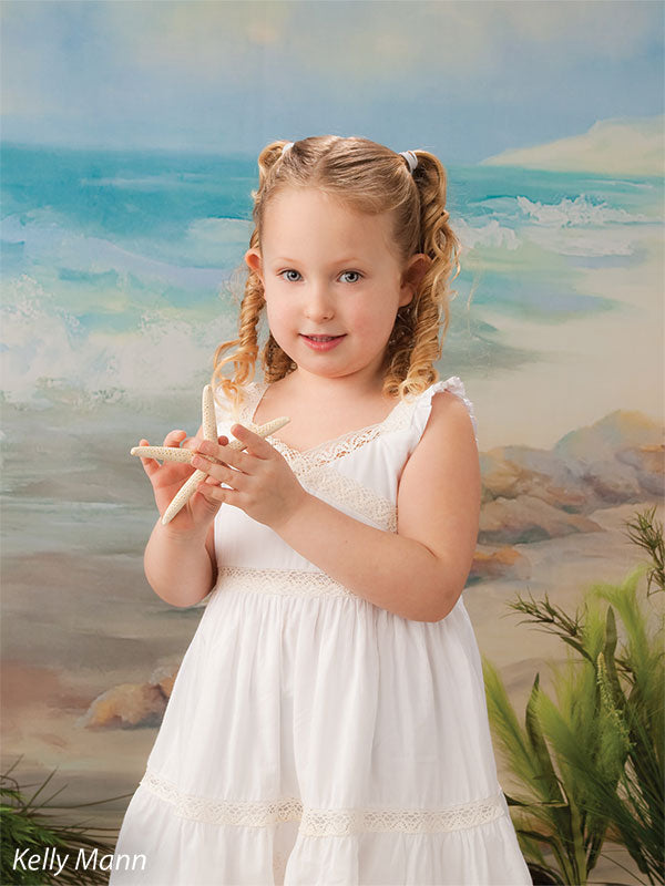Child portrait with beach backdrop featuring waves and rocks, suited for family and school photos with ocean-inspired styling.