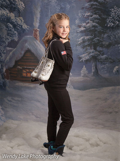 The Holiday Cottage backdrop sets a peaceful wintry mood behind a girl holding skates in a cozy holiday portrait.