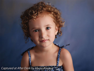 Close-up portrait of child with soft curls in front of neutral blue Venetian backdrop, ideal for family, school, and milestone portraits.